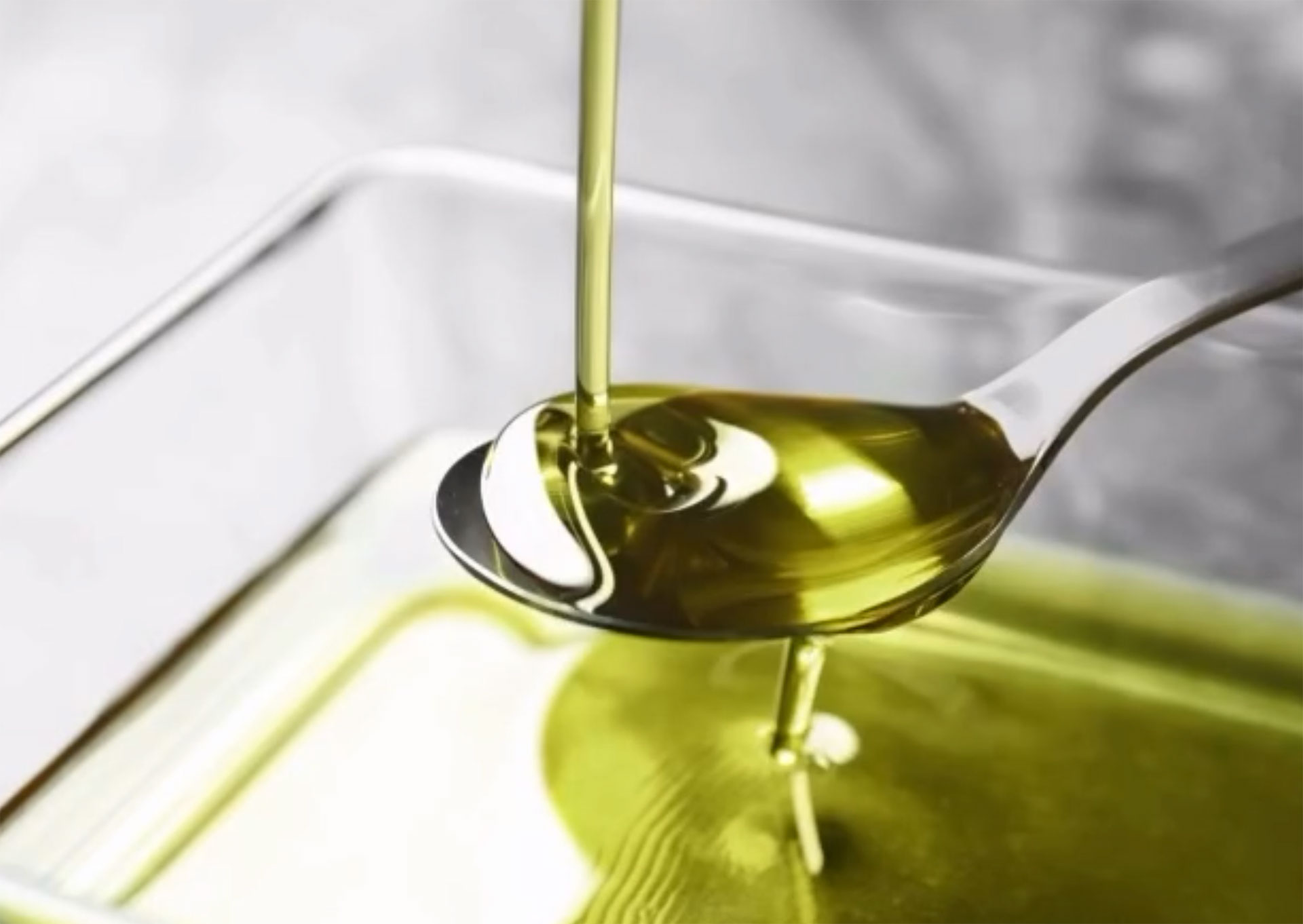 Aceite de oliva virgen extra cayendo desde una cuchara sobre fondo oscuro